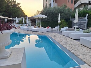 A swimming pool with white lounge chairs and umbrellas, surrounded by stone flooring and greenery. - Biancopineta B&B (San Salvo)