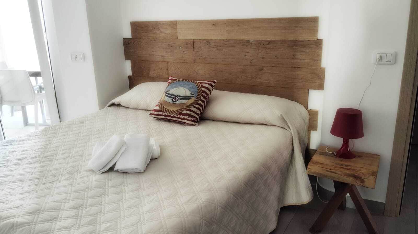 Ein Bett mit einer gesteppten Tagesdecke, ein Kopfkissen mit Meeresmotiven und eine rote Lampe auf einem Nachttisch.
