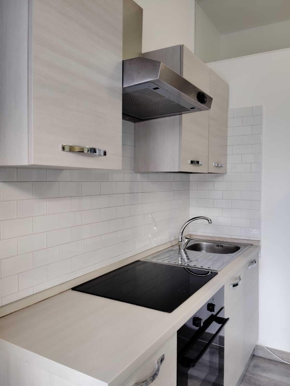 A modern kitchen with a black countertop, stainless steel sink, and light-colored cabinets.
