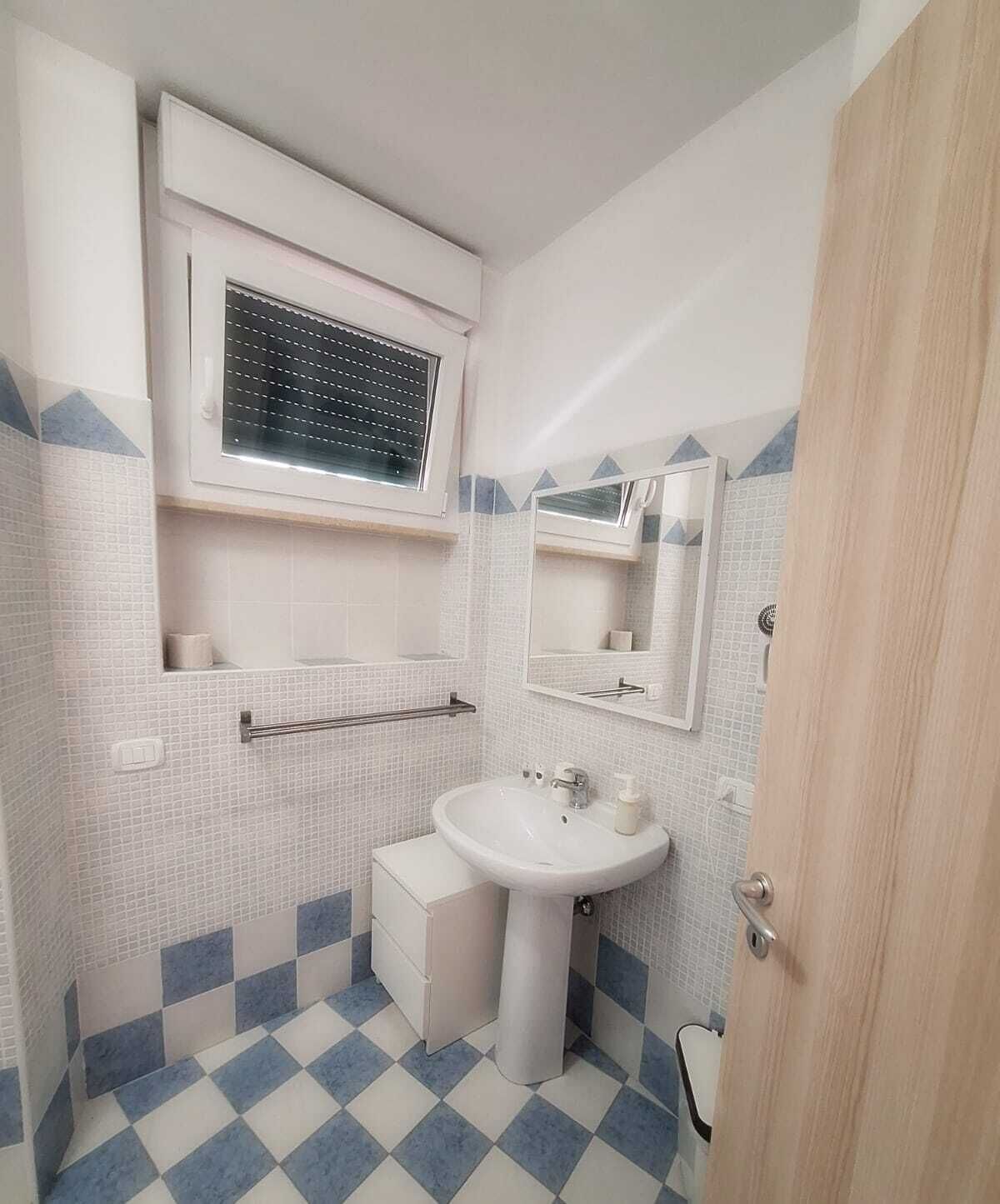 A bathroom with a white sink, a mirror, and a window with blinds.