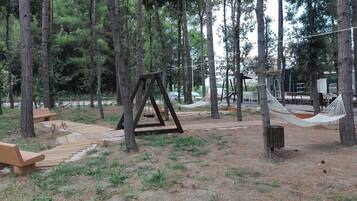 Un área boscosa con un columpio de madera, mesas de picnic y una hamaca.