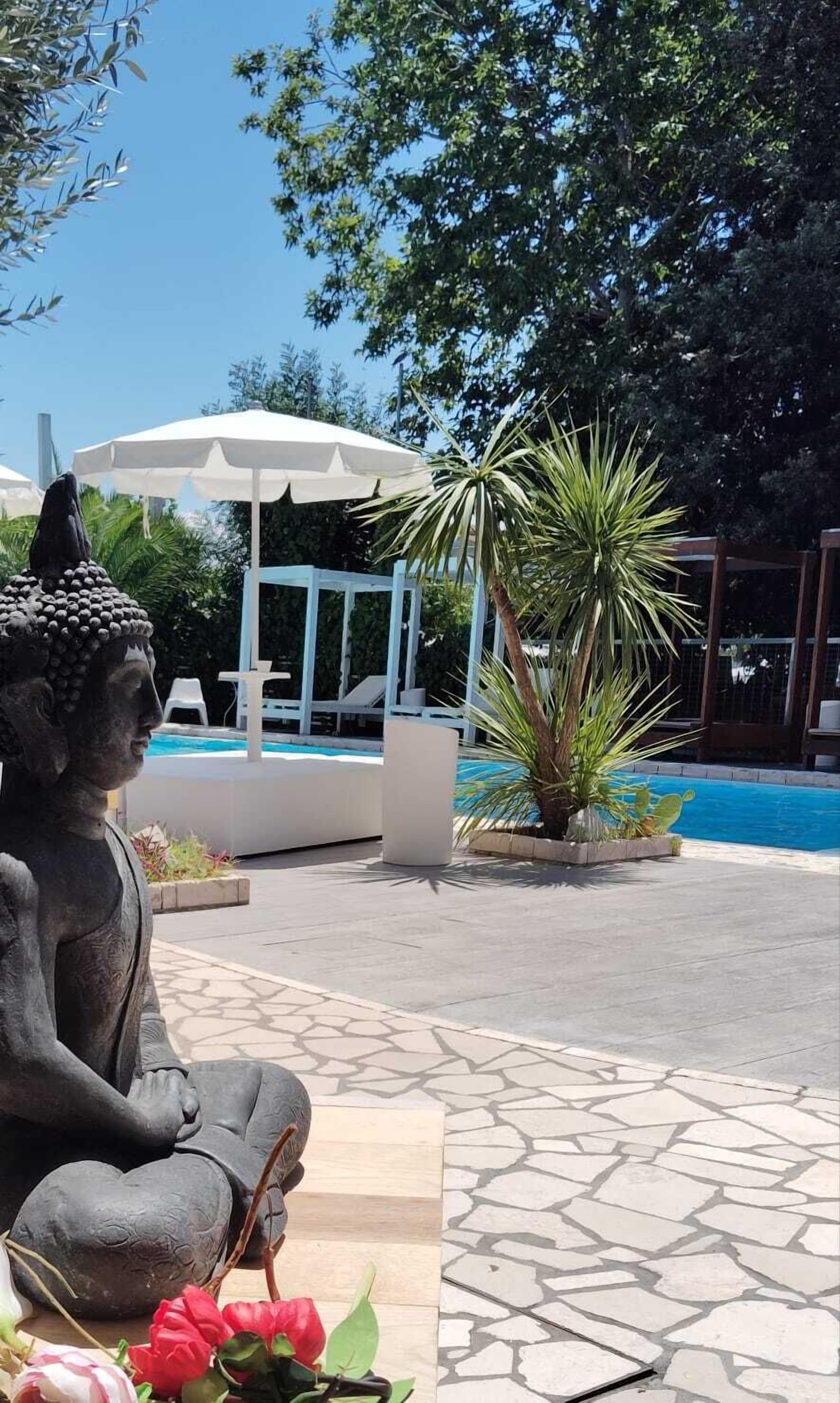 Eine Statue einer sitzenden Person, ein Schwimmbecken und umliegendes Grün.