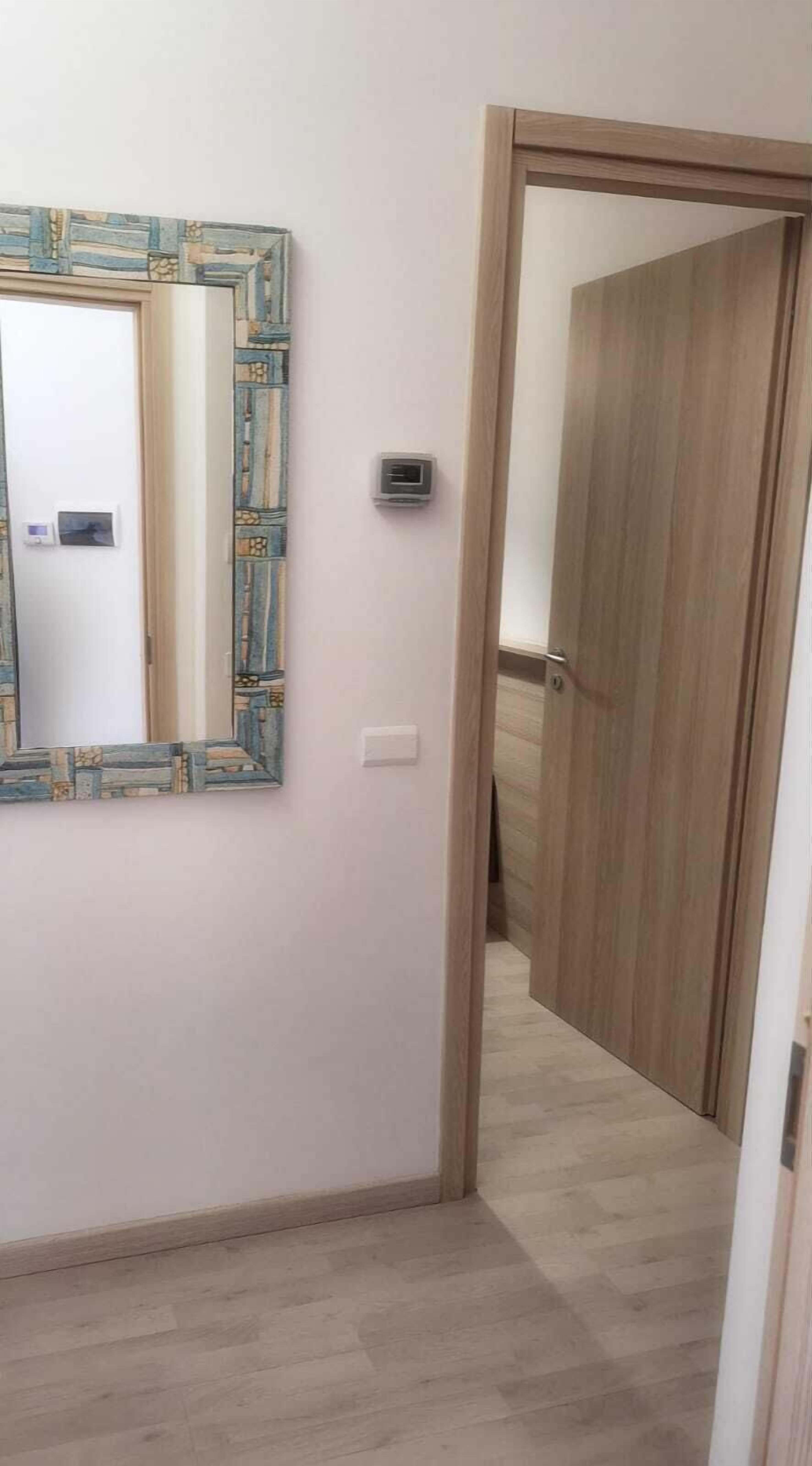 A hallway with a patterned mirror, a light switch, and a door leading to another room.