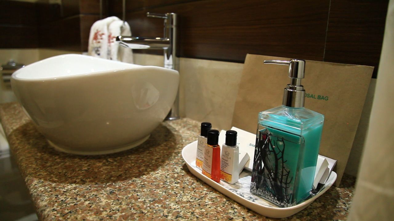 A bathroom with a large white bathtub, a sink with a silver faucet, and a soap dispenser on a tray.