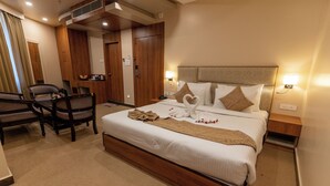 A hotel room with a large bed, wooden headboard, two bedside tables with lamps, a desk with a chair, and a wardrobe. - Hotel Heiga (Shillong)