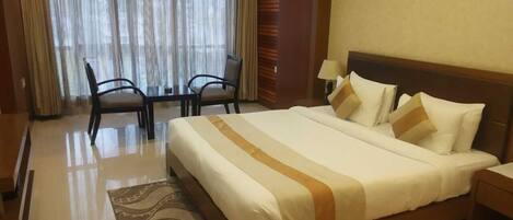 A hotel room with a large bed, a desk, two chairs, and a window with curtains.