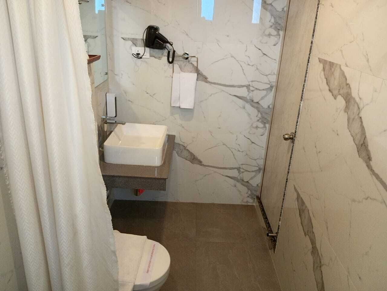 A bathroom with a marble wall, a sink, a towel rack, and a shower area.