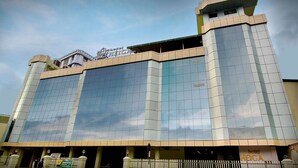 A modern hotel building with a prominent glass facade and a rooftop sign. - Hotel Heiga (Shillong)