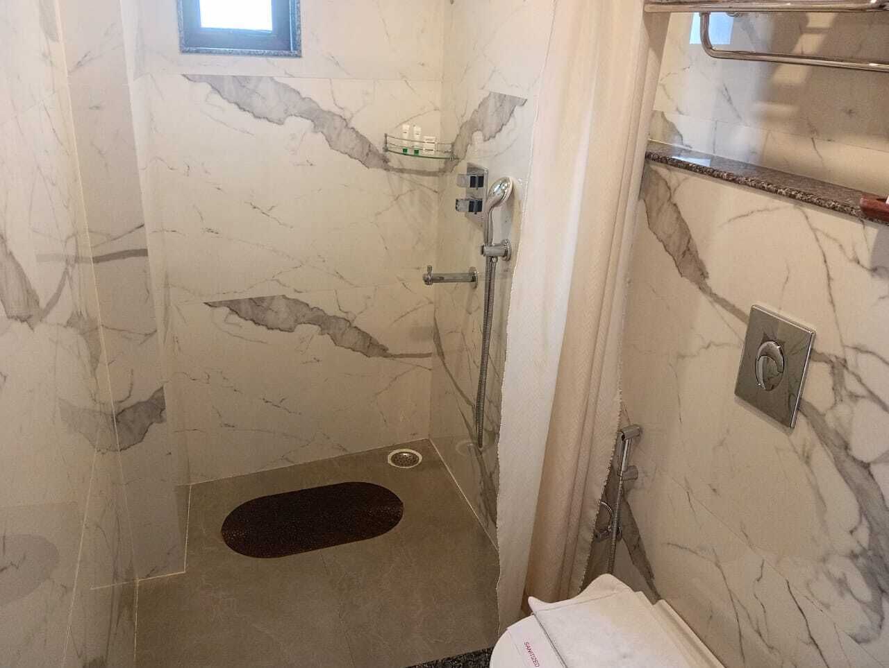 Ein kleiner, abgeschlossener Duschbereich mit Marmorwand, Duschbrause und Handwascharmatur.