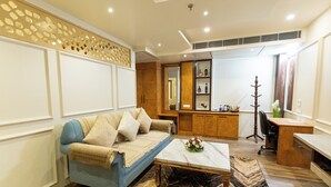 A modern living room with a blue sofa, a coffee table, and a wooden desk. - Hotel Heiga (Shillong)