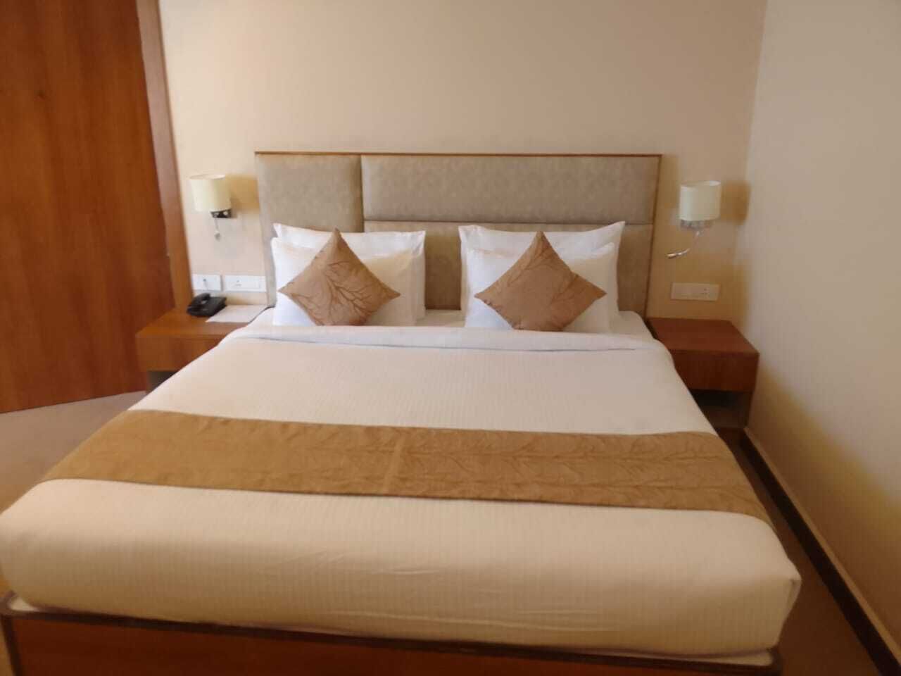 A neatly made bed with a beige headboard, two bedside tables with lamps, and a brown throw blanket.