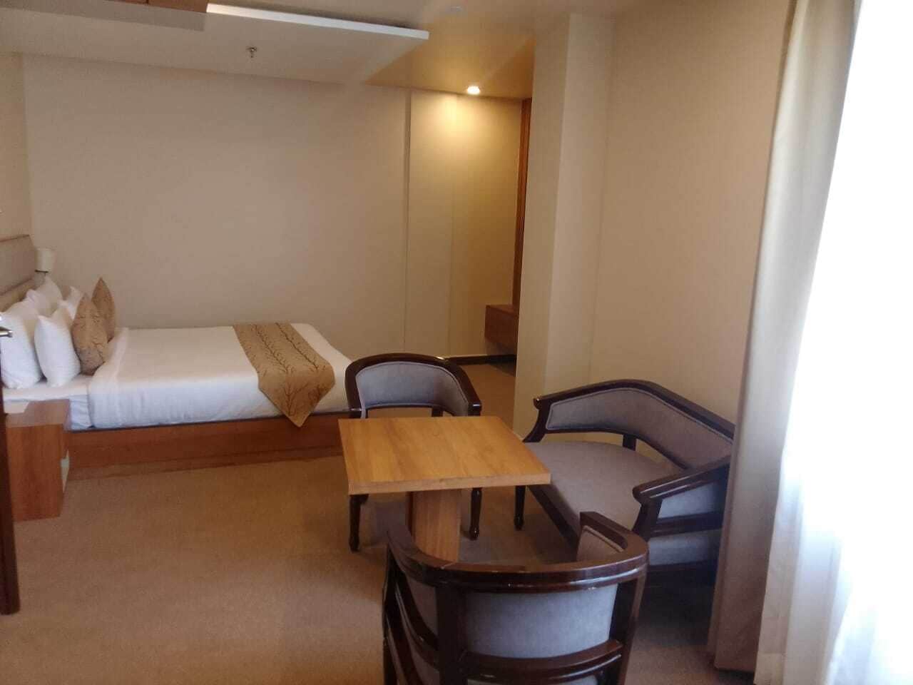 A compact room with a bed, a small table, two chairs, and a bedside table with a lamp.