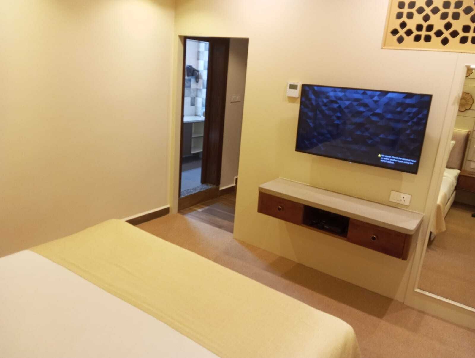 A hotel room with a bed, a TV mounted on the wall, and a small wooden cabinet below it.