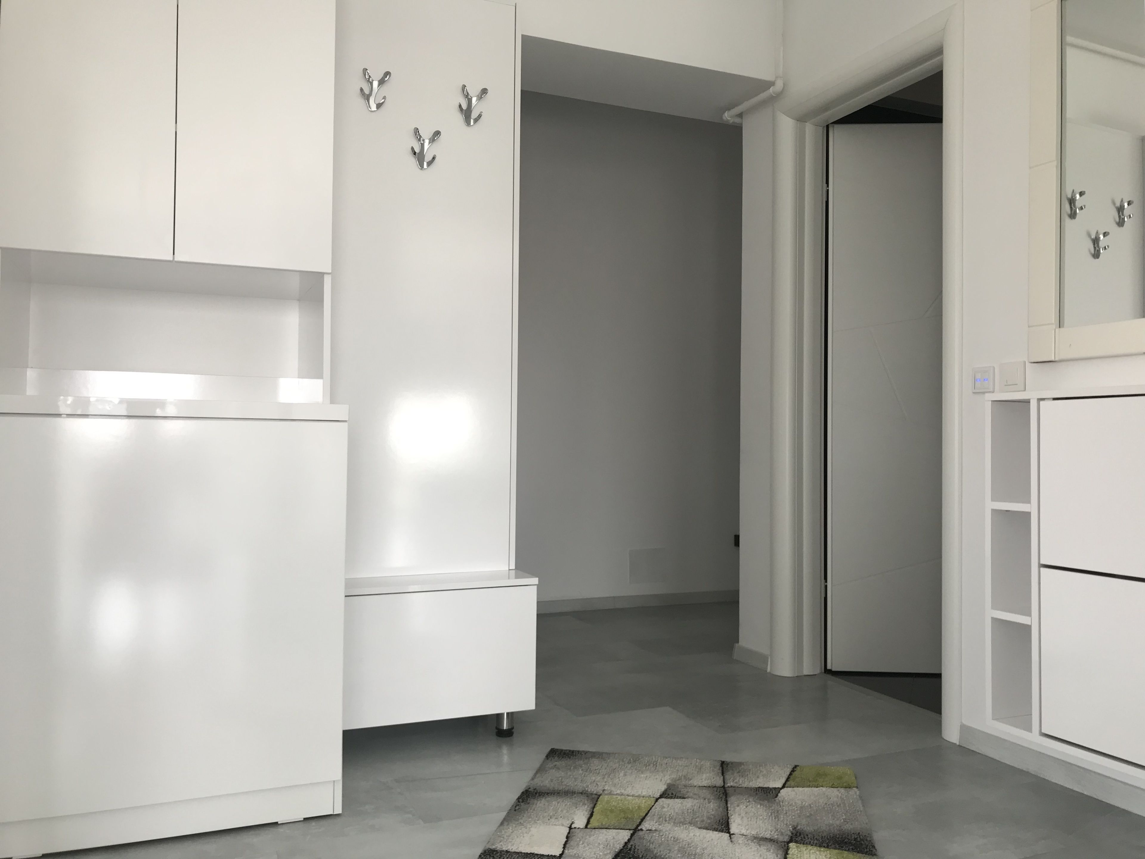 A modern, minimalist room with white cabinetry, a patterned rug, and a door leading to another room.