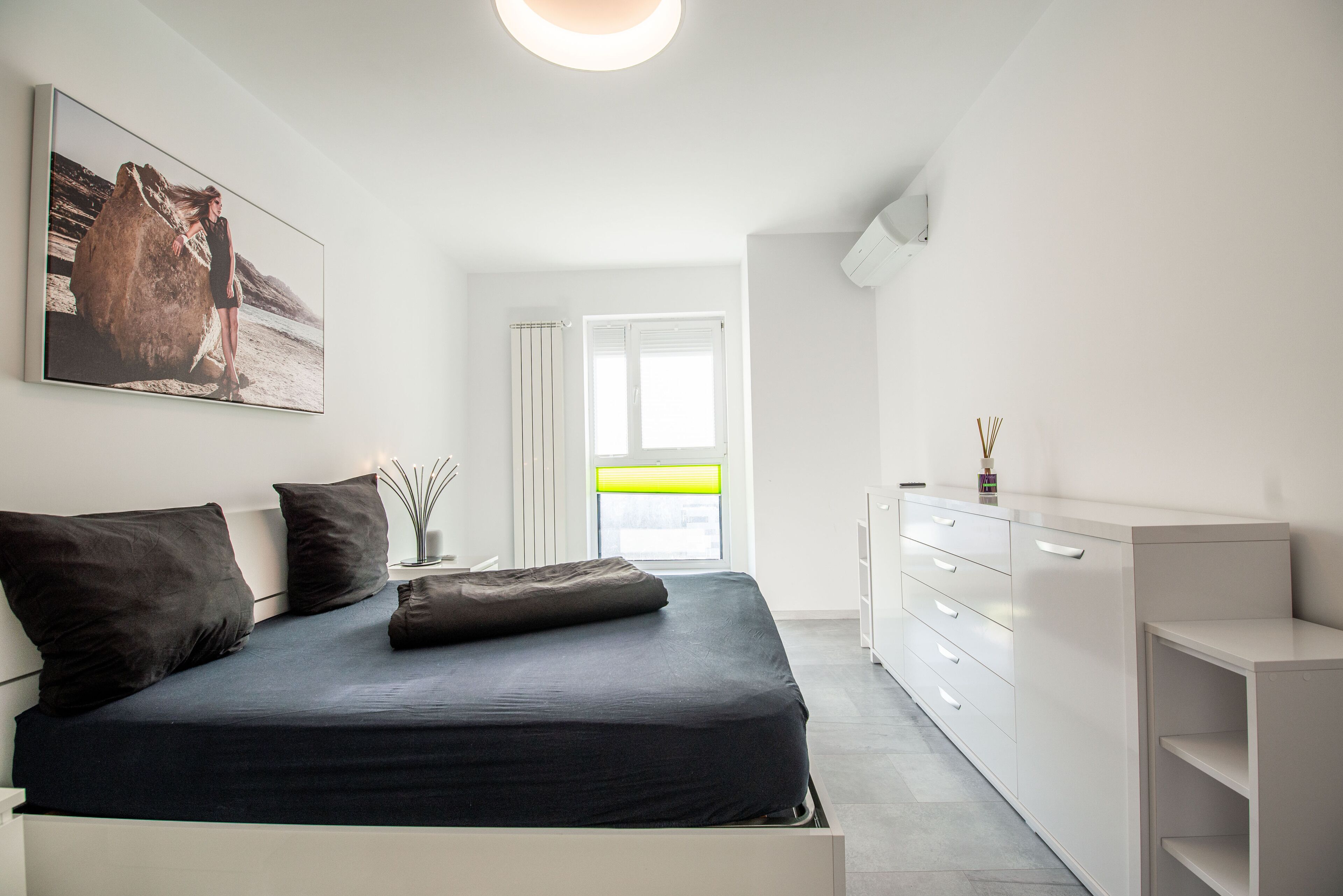 A modern bedroom with a large bed, a bedside table, a dresser, and a window with a view.