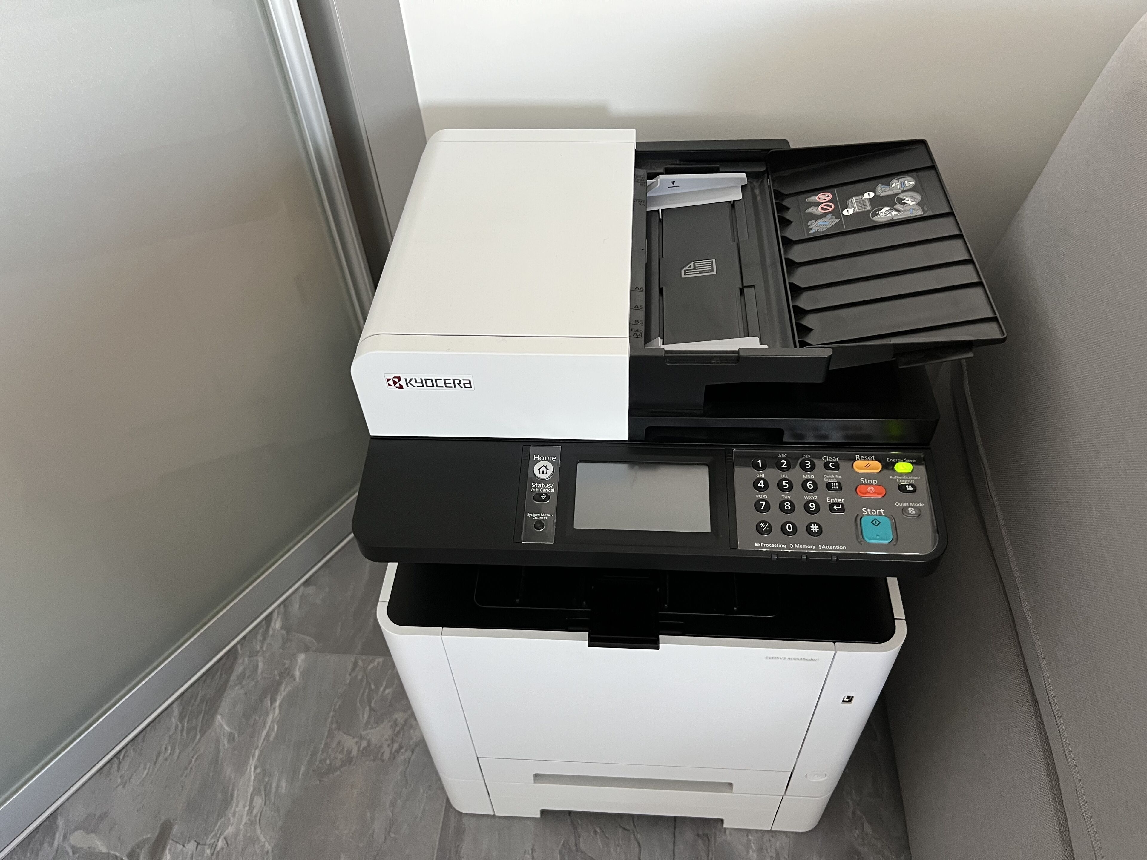 A Kyocera multifunction printer with a control panel, a paper tray, and a document feeder.