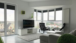 A modern living room with a flat-screen TV, a grey sofa, a black chair, and a round green decorative piece. - Luxury Westpark 2 Residence Lake View W2 (Bucharest)