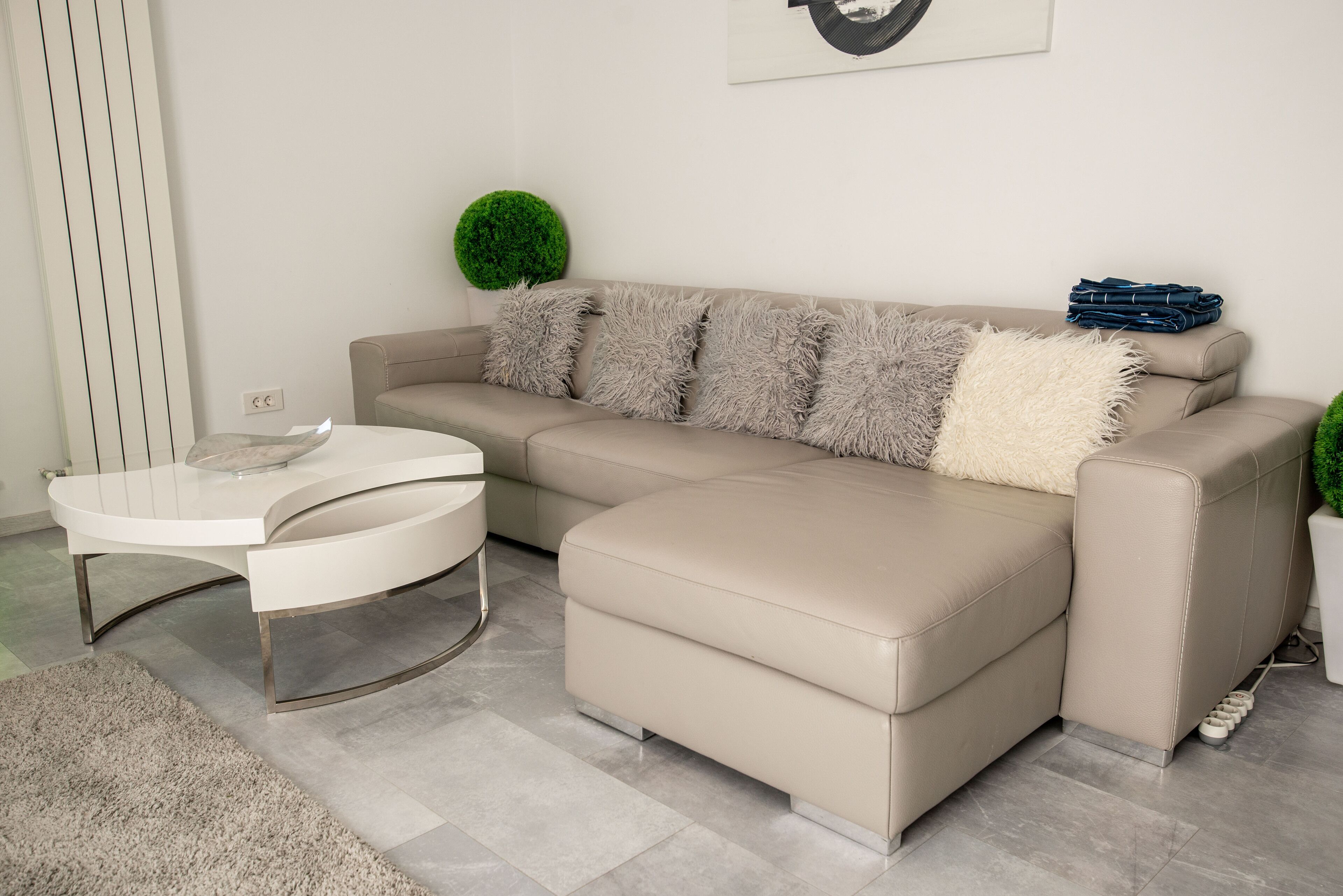 A modern living room with a beige sectional sofa, a white coffee table, and a green decorative round plant.
