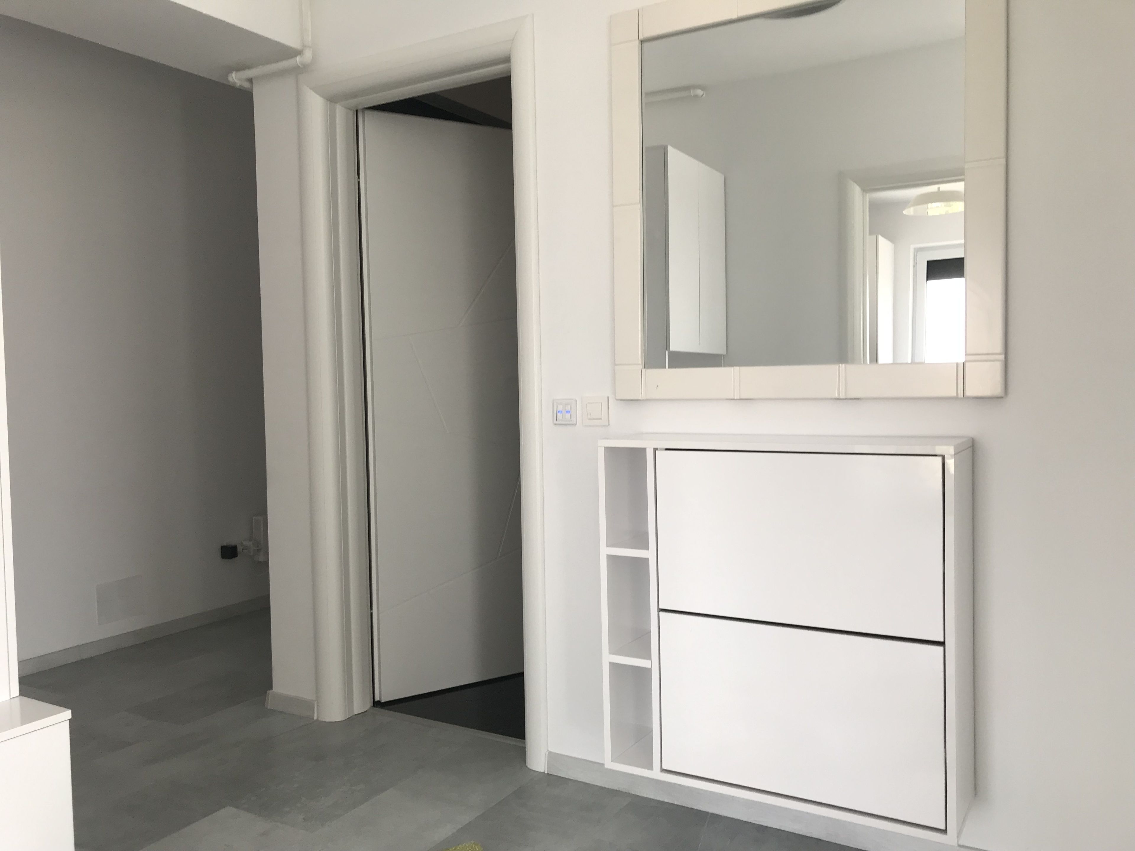 Um banheiro moderno e minimalista, com um espelho grande, um armário embutido e uma porta que dá para outro cômodo.