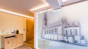 Een hal met een houten kast, een ingelijst architectuurtekening aan de muur, en een deur.