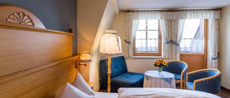 Una habitación de hotel con cama, escritorio, silla y ventana con cortinas.