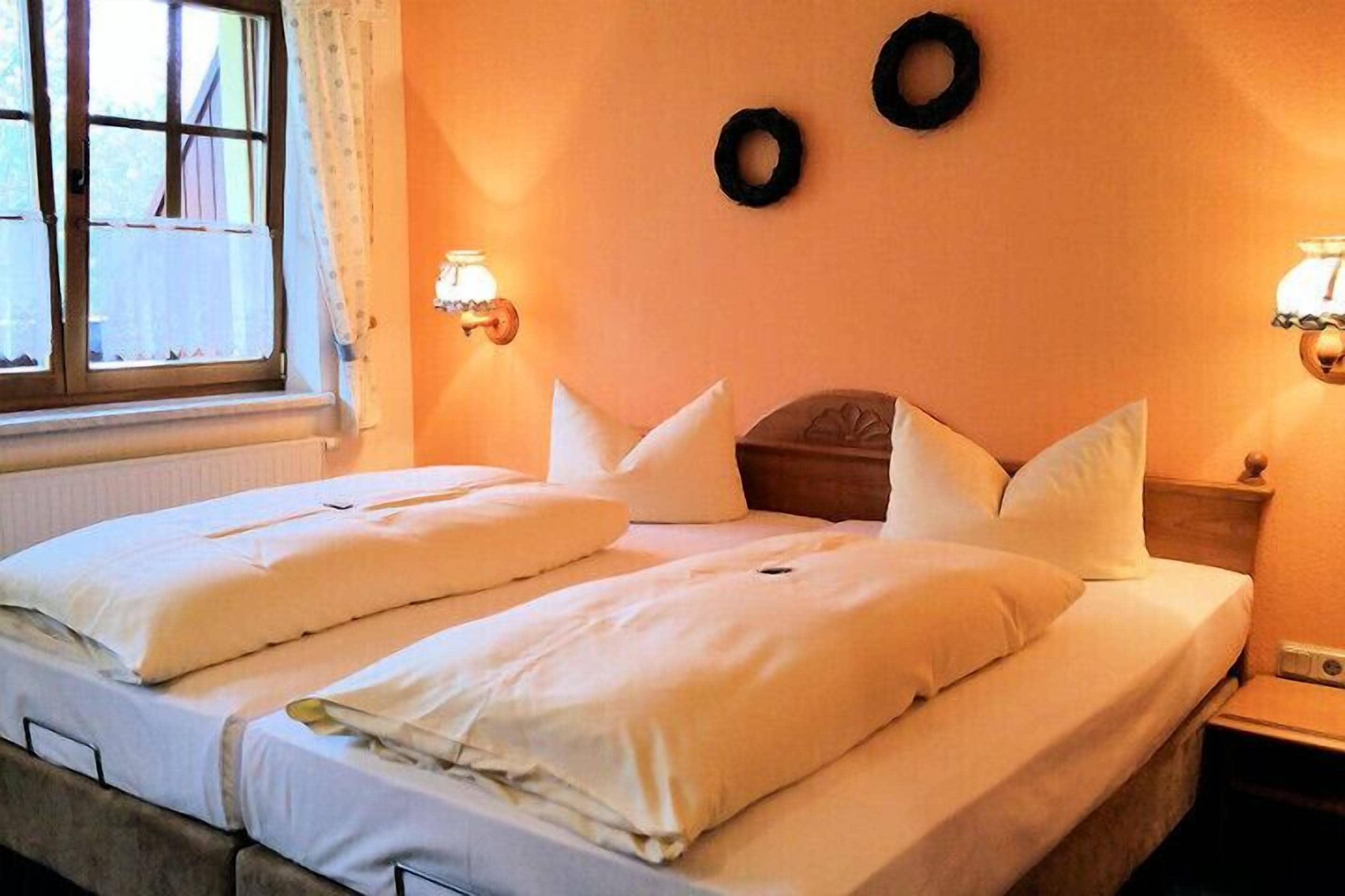 A double bed with white linens, two wall-mounted lamps, and a window with curtains.