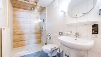 Un baño moderno con cabina de ducha de madera, inodoro blanco, lavamanos con dispensador de jabón y un espejo grande.