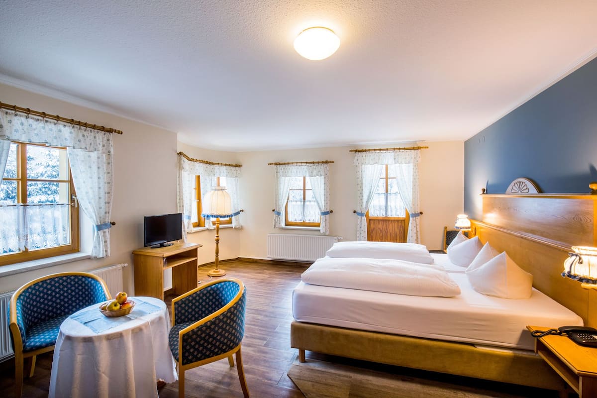 A hotel room with a bed, two chairs, a small table with fruit, and a TV.
