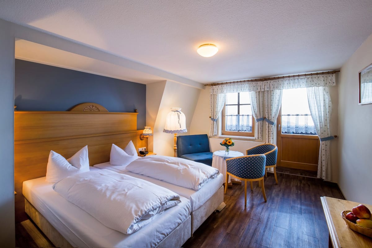 A hotel room with a bed, a chair, a small table, and a window with curtains.