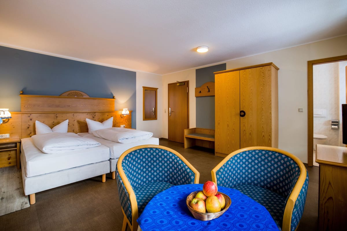 A hotel room with two beds, a dining table with chairs, and a fruit basket.