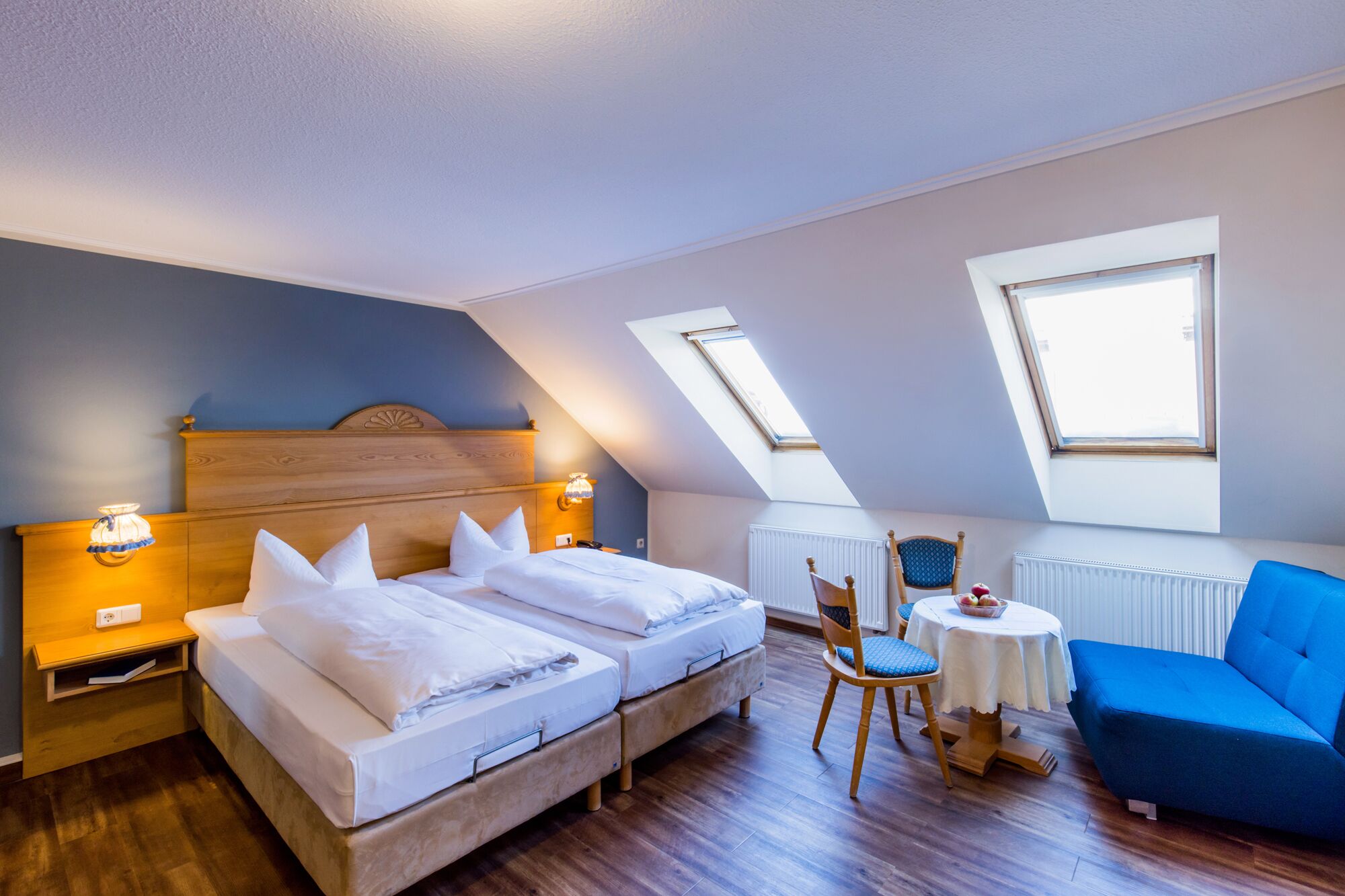 Une chambre à coucher avec un lit, deux tables de chevet, une chaise, une petite table et un canapé bleu.