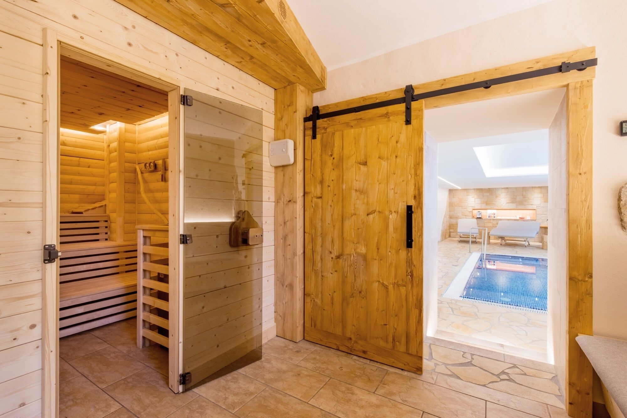 A wooden cabin interior with a sauna, a stone-tiled floor, and a view of an outdoor swimming pool.