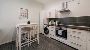 A compact kitchen with a washing machine, oven, and a small dining area with chairs. - *Renovated* Dilo Apartments - MyGold - Large 120-square-meter apartment, 2 bedrooms, with a balcony (Berlin)