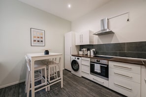 A compact kitchen with a washing machine, oven, and a small dining area with chairs.