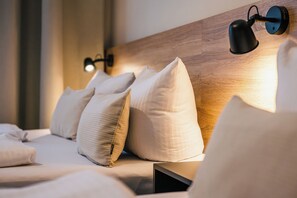 A neatly made bed with pillows, a wooden headboard, and two wall-mounted reading lamps.