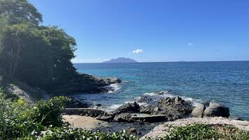 Un paysage côtier caractérisé par des rivages rocheux, une eau d’un bleu limpide et une chaîne de montagnes à l’horizon.