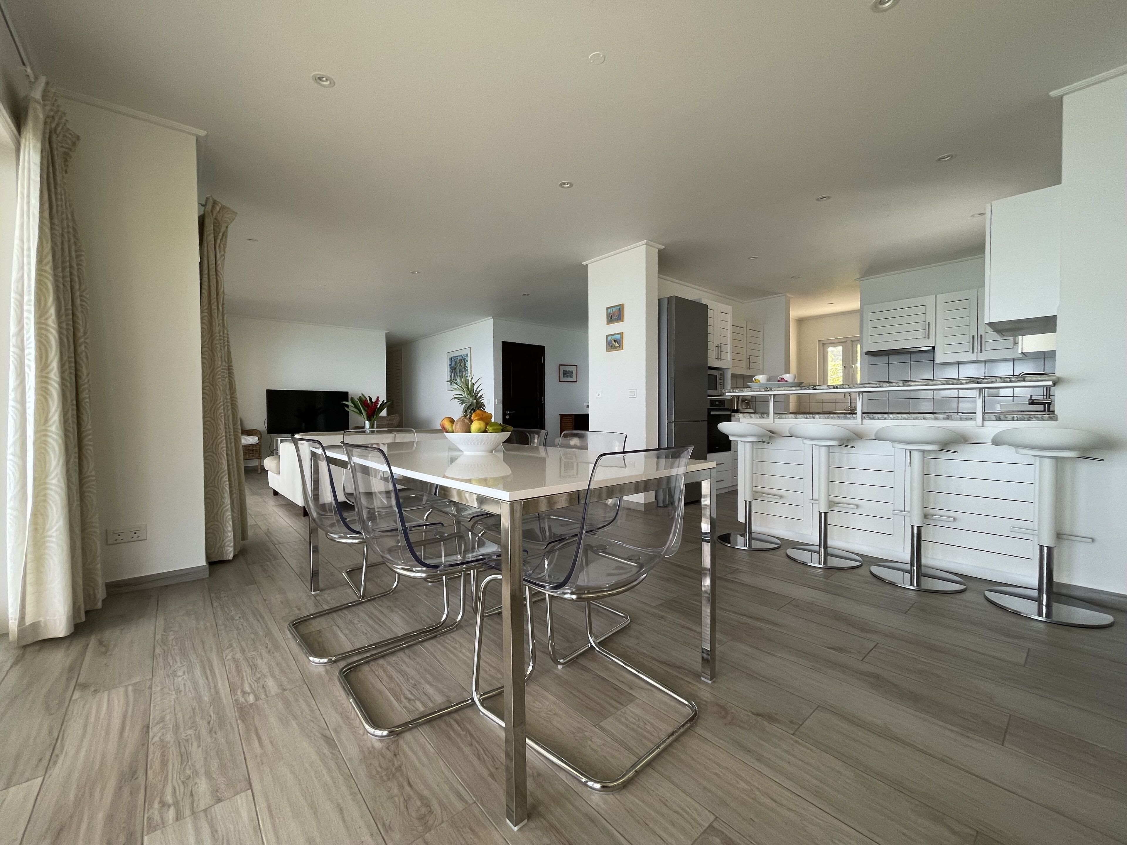 A modern kitchen with a central island, bar stools, and a dining area with clear chairs.