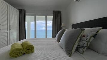 Een hotelkamer met een bed, uitzicht op zee en een raam met gordijnen.