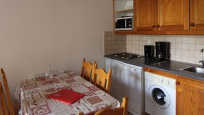 Een kleine keuken met houten kastjes, een magnetron, een koffiezetapparaat, een wasmachine en een tafel met een rode map.