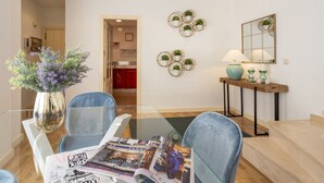 A modern living room with a glass coffee table, two blue armchairs, a wooden side table with a lamp, and decorative wall art. - Genteel Home Francos Terrace VI (Sevilla)