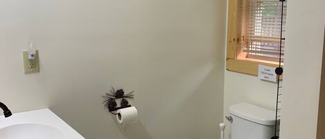 A small bathroom with a white sink, toilet, and a window with blinds.