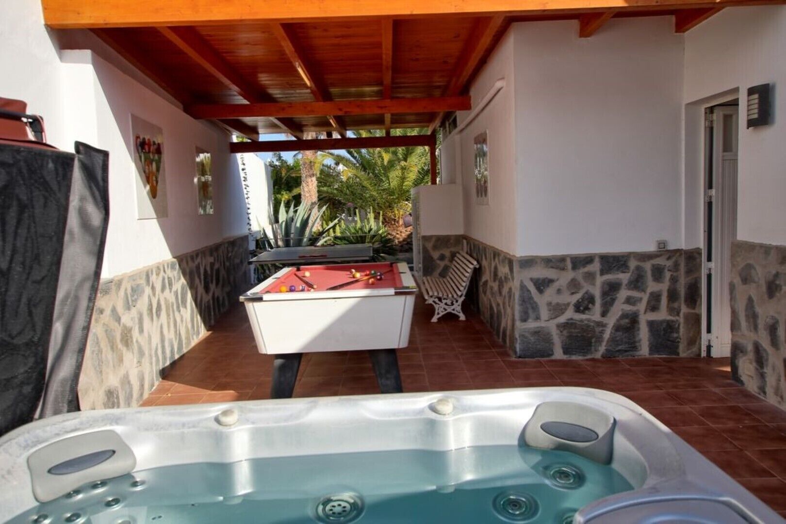 A pool area with a hot tub, a pool table, and a stone wall.
