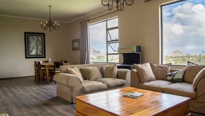 Amplia sala de estar con una mesa de centro de madera, sofás color beige, un comedor con mesa y sillas, un ventanal con vista a la montaña y un candelabro.