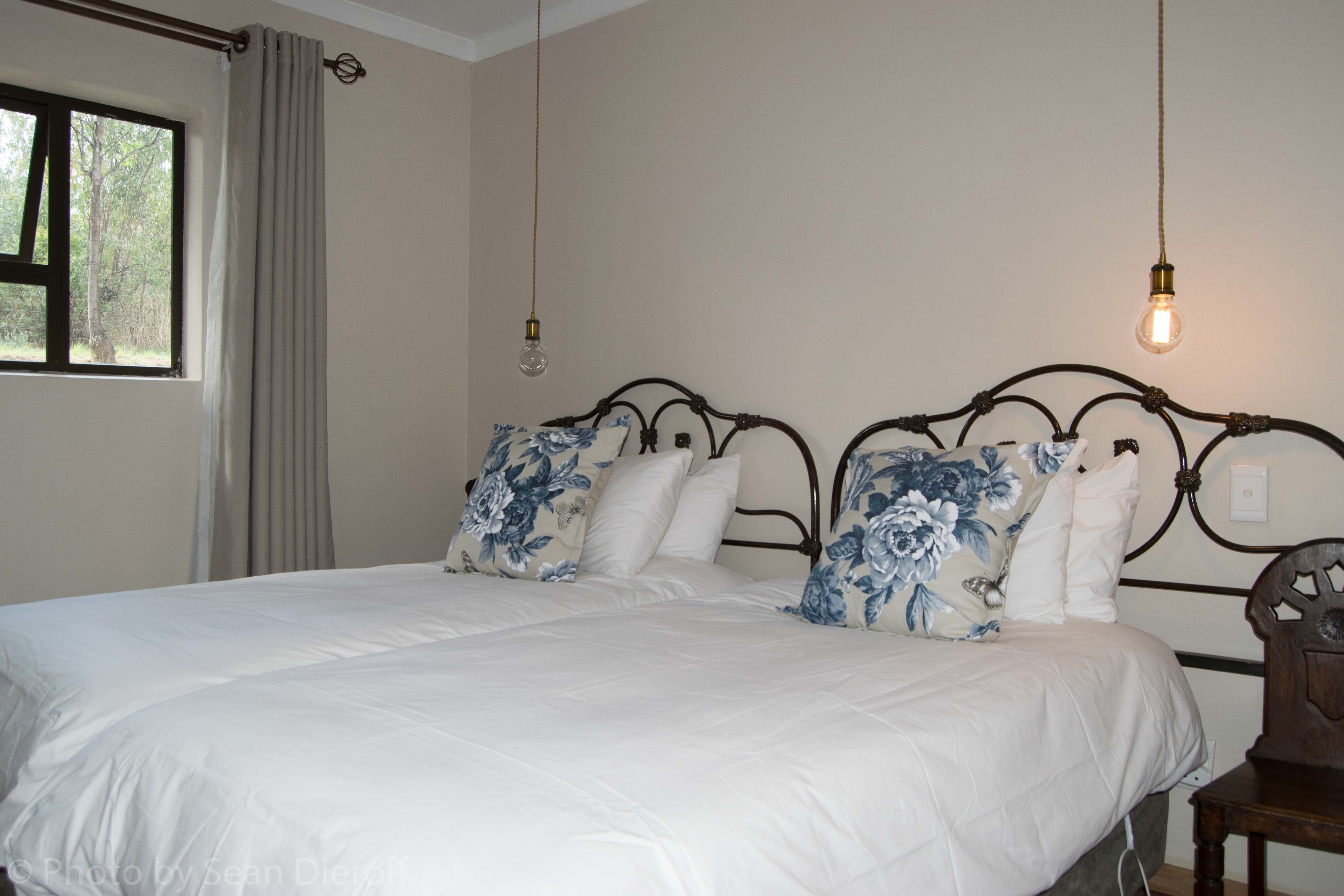 A bedroom with a large bed, two pillows, a headboard, a window with curtains, and a hanging light fixture.