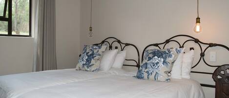 A bedroom with a large bed, two pillows, a headboard, a window with curtains, and a hanging light fixture.