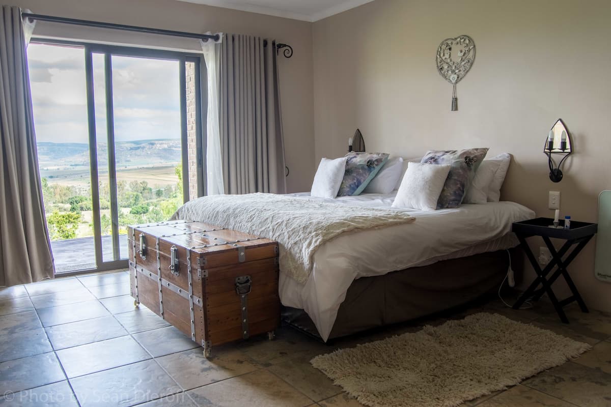 A bedroom with a large bed, a wooden chest, and a view of the countryside through a sliding door.
