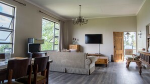 Un salón amplio con sofá, mesa de comedor, sillas, televisor de pantalla plana y una lámpara de araña.