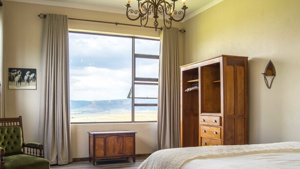 Un dormitorio con una cama grande, un armario de madera, un sillón verde, una mesita pequeña y vistas a la playa a través de una ventana.