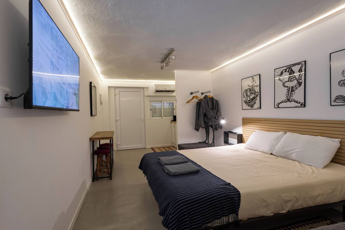 Een slaapkamer met een bed, een aan de muur bevestigde televisie en kunstwerken op de muren.