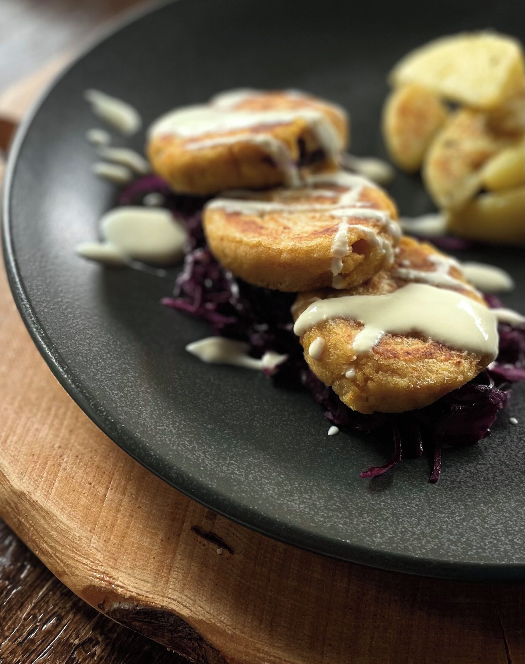 Un plato con distintos alimentos, entre ellos unas empanadas fritas y una salsa cremosa, sobre un plato oscuro y con un fondo de madera.